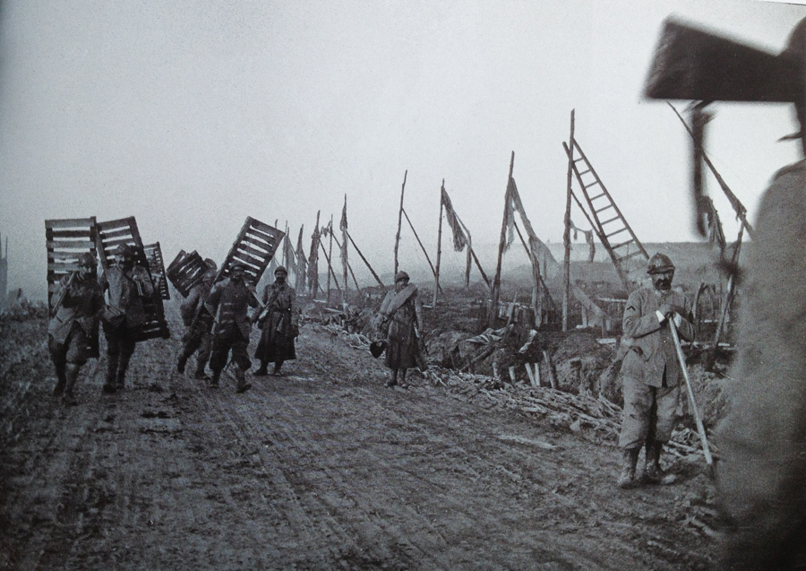 A group of soldiers carries duckboards up to the front lines. The road shows signs it was once well camouflaged before it was heavily bombarded. Photo taken by Frantz Adam, near Verdun, October 1917.