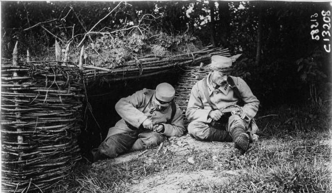 Two soldiers making trench rings in their spare time in front of their shelter.