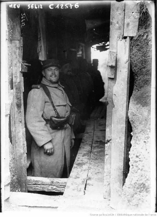 A soldier smiles at the photographer as he stands with his comrades in a covered trench, early 1915.