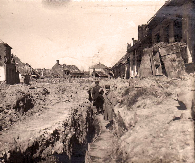 A trench cuts through the street of a devastated village, ca. 1915. 