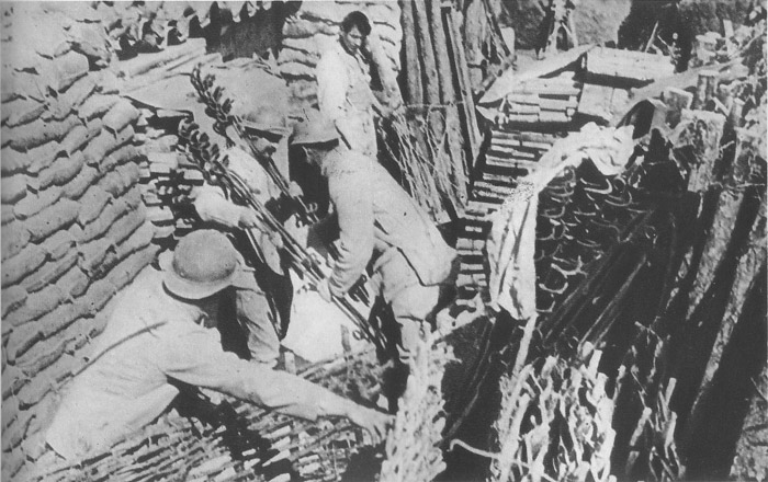 A supply dump in a support trench--sections of wattling, sandbags, iron barded-wire stakes.