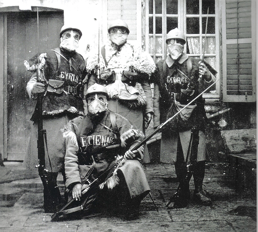 A group of soldiers donning TN gas masks and sheepskins presents a truly strange sight. An incredible juxtaposition of antiquity and modernity. The men have written their names in chalk to identify themselves. (Dec. 1915)