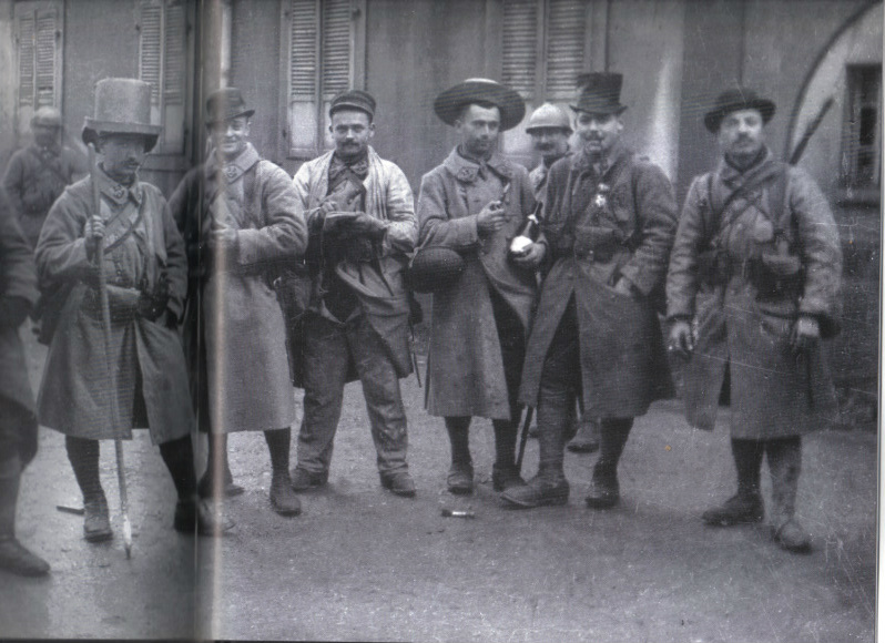 Soldiers requisition a set of fine hats in an abandoned village. One, lacking anything finer, is even wearing a hat box.