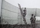 Canvas netting is erected along a roadway to prevent aerial observation as part of the preparations of the Chemin-des-Dames offensive. Photo taken by Frantz Adam, near Villers-Franqueux, March 1917.