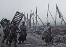 A group of soldiers carries duckboards up to the front lines. The road shows signs it was once well camouflaged before it was heavily bombarded. Photo taken by Frantz Adam, near Verdun, October 1917.