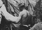 A soldier combs his clothes for lice beside his trench shelter.