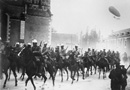 Chasseurs à cheval parade through town while a dirigible flies overhead in 1914.