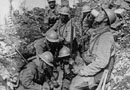 Men of the 152 RI rest after an attack in Argonne and share a cup of pinard. Note the early style raquette grenades suspended from the belt of the man on the right and the shell lodged in the tree.