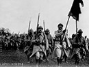 A column parades past the camera with regimental colors unfurled.