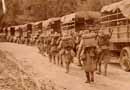 Troops march by a idle convoy of trucks.