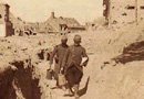 A ration party carries food along a trench that cuts through a town.