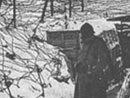 A soldiers stands in a snowy trench completely covered with barbed wired.
