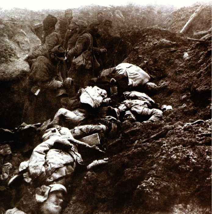 Photo taken in a conquered German trench just after an attack in early 1915. Amongst the dead one man collects German helmets as souvenirs.