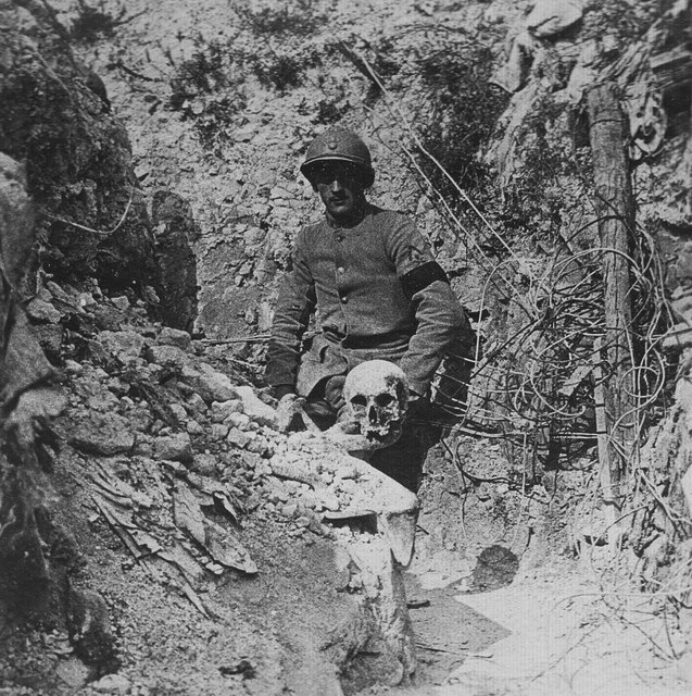 A French soldier wearing a mourning arm band poses beside a skull. 