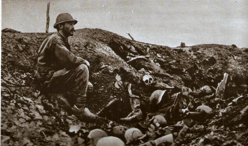 French soldier in the remains of a trench, huddling among piles of German dead. 