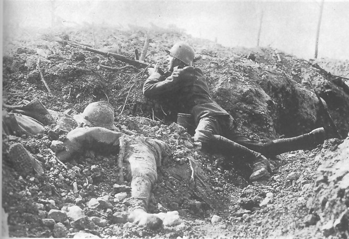 German rifleman takes cover next to some half-buried French corpses.